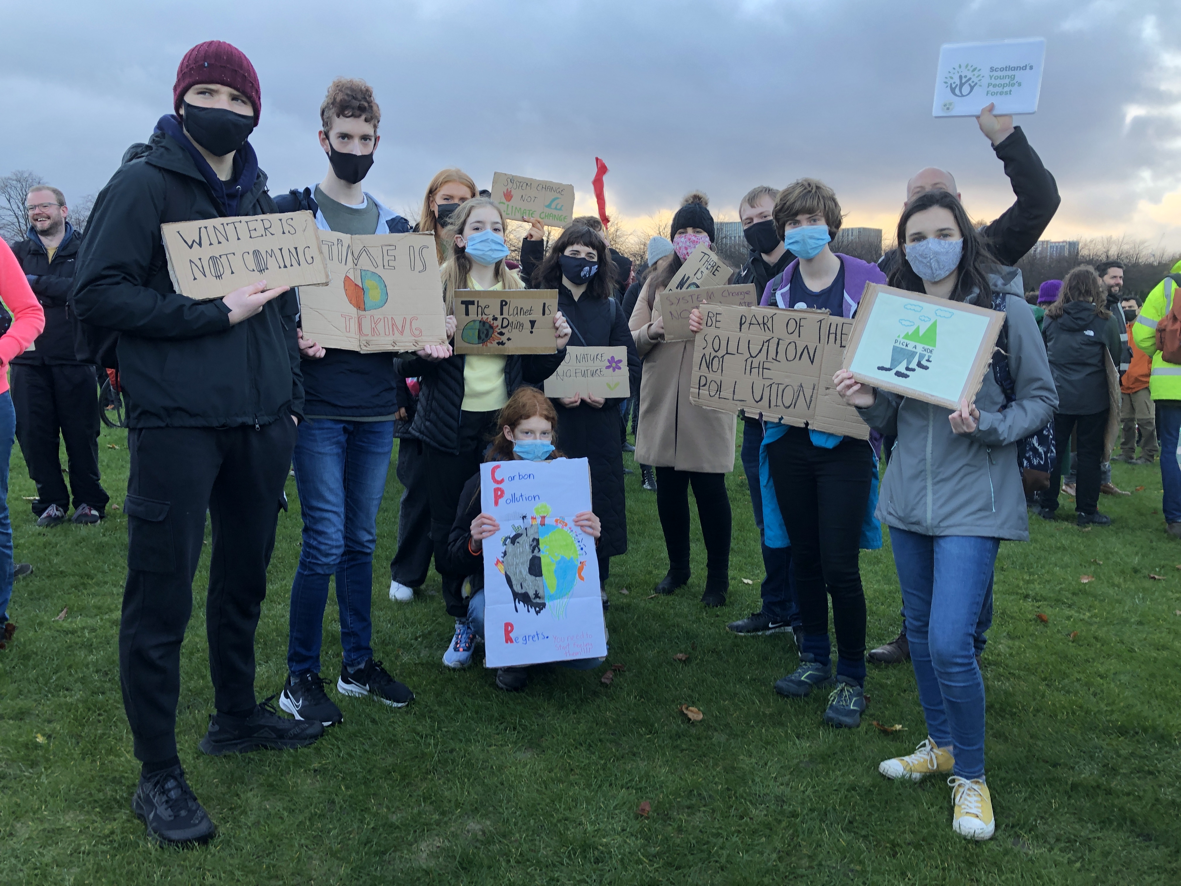 一群年轻人一起站在草地上，每人举着与气候变化有关的标语牌